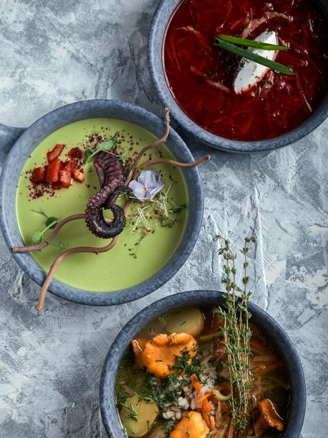 Gray plates with different soups on a gray background. Plate with asparagus soup with octopus, a plate of traditional borscht with sour cream, a plate with mushroom soup and standing on multi-colored linen napkins on a concrete marble gray background. Gray light texture background close-up top view. Beautiful table setting
